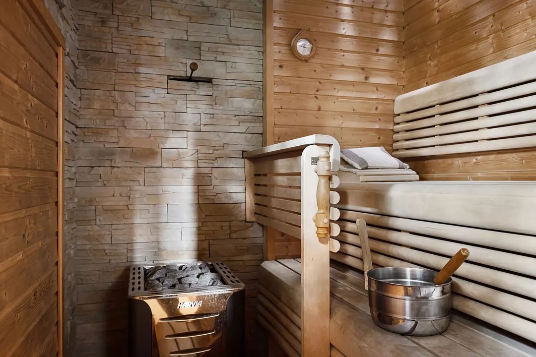 sauna - A small sauna with an electric Harvia heater, a steel water bucket and a long-handled ladle resting on the bench